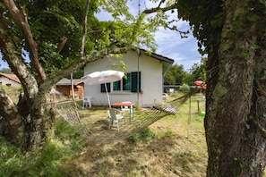 A house with a hammock, a table, and a chair in the yard. - Charming Country Cottage with Shared Garden (Hourtin)
