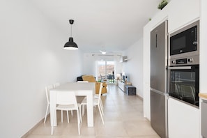Eine moderne Küche mit Einbauofen und Mikrowelle, eine Essecke mit Tisch und Stühlen sowie ein Blick durch ein Fenster.