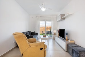 Ein modernes Wohnzimmer mit einer Couch, einem Couchtisch, einem Fernseher und einem Balkon mit Blick.