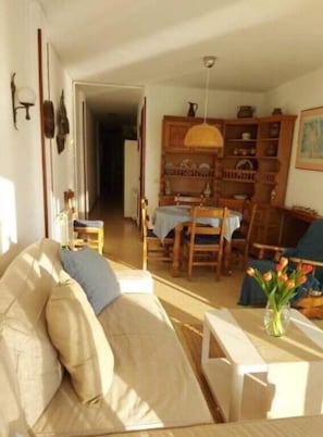 Una sala de estar con un sofá, una mesa de comedor con sillas, una estantería y una lámpara colgante.