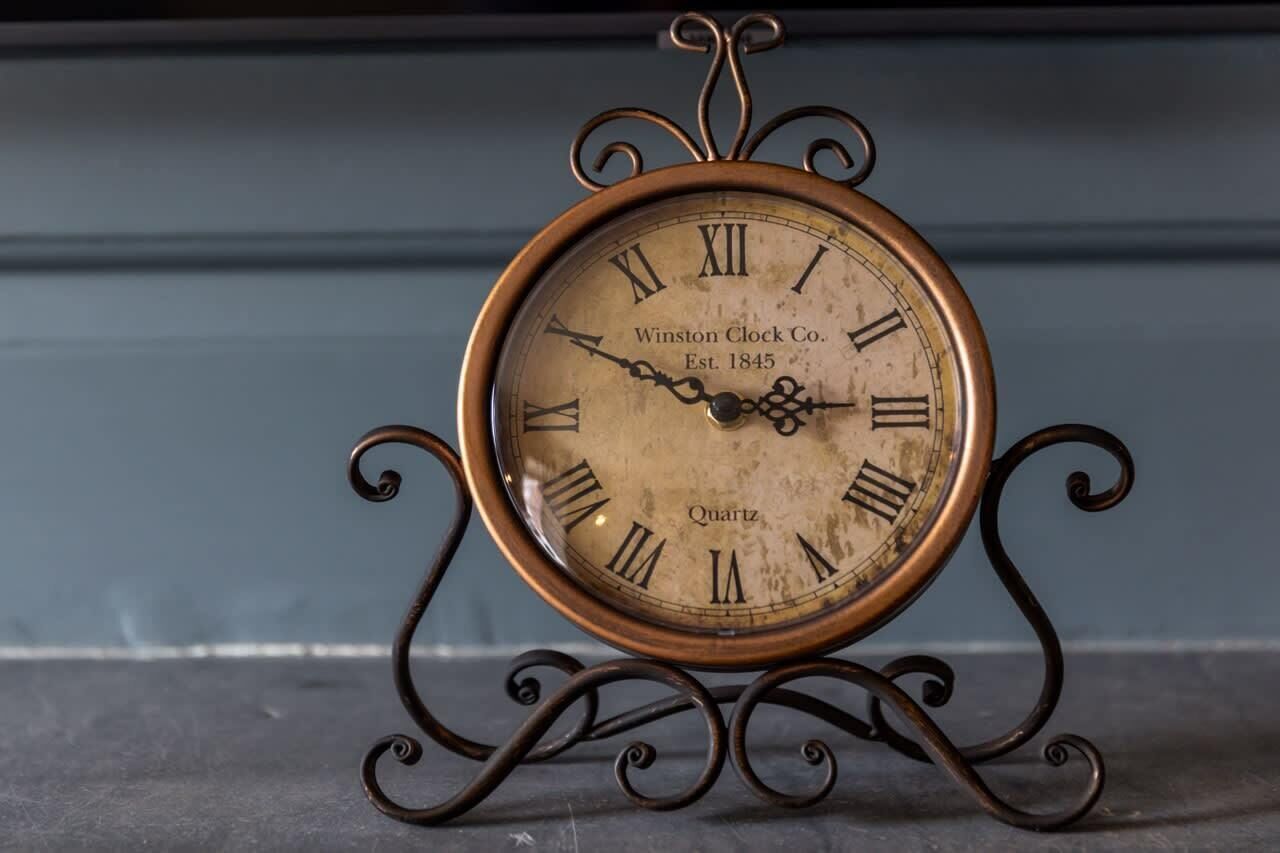 Une horloge ancienne avec des chiffres romains, un cadre en laiton et un support décoratif.