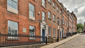 Une rangée d’immeubles en briques rouges aux encadrements de fenêtres blancs, une rue pavée et une clôture en métal noir.