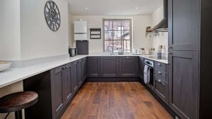Une cuisine moderne avec des meubles de couleur sombre, une grande fenêtre et une horloge décorative au mur.