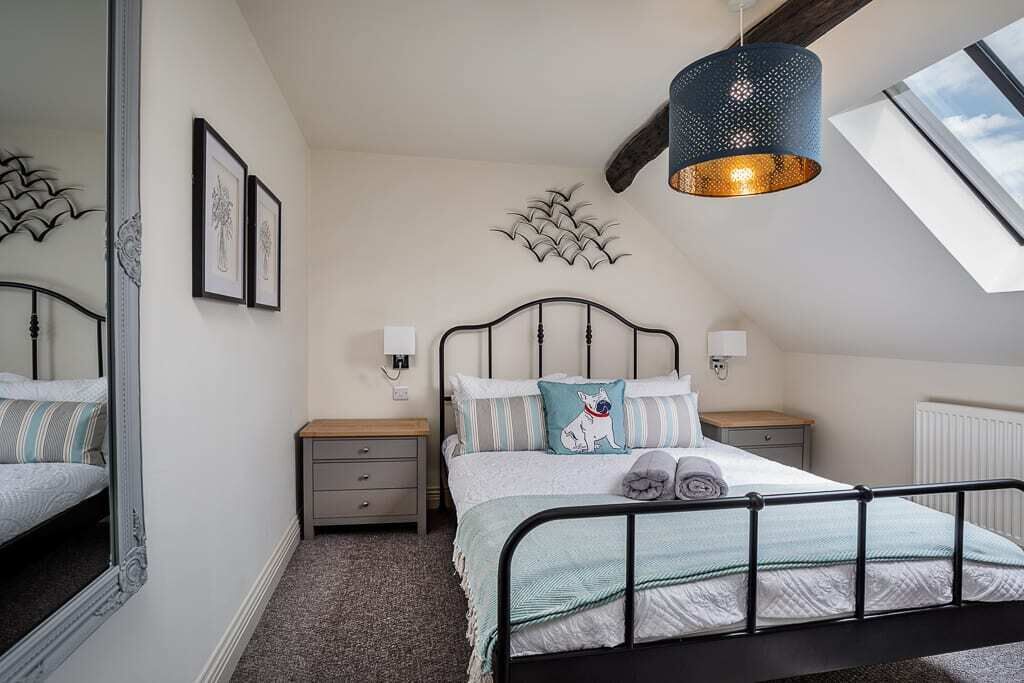 A bedroom with a bed, bedside tables, wall art, a ceiling light fixture, and a skylight.