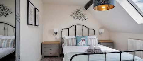 A bedroom with a bed, bedside tables, wall art, a ceiling light fixture, and a skylight.