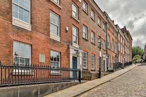 A row of red brick buildings with white window frames, a cobblestone street, and a black metal fence.