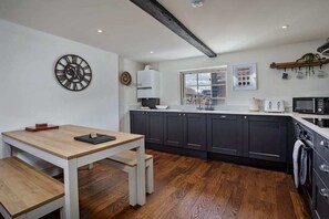 Een moderne keuken met donkere kastjes, een houten tafel en een grote wandklok.