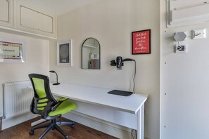 A white desk with a black lamp, a green and black office chair, a framed mirror, and a red motivational quote on the wall.