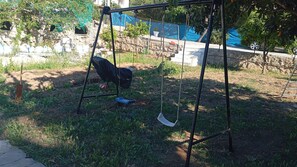 A swing set in a grassy area with a stone wall and trees in the background. - Holiday Home 'Calafell' with Mountain View, Wi-Fi and Air Conditioning (SEGUR DE CALAFELL)