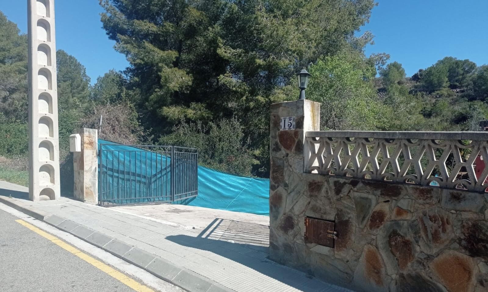 A stone wall with a metal gate, a blue tarp, and a clear sky.