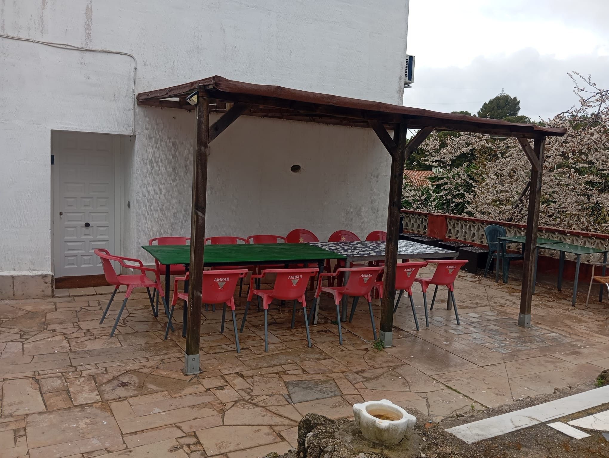 Un patio al aire libre con una mesa y sillas, una pérgola y un edificio blanco al fondo.