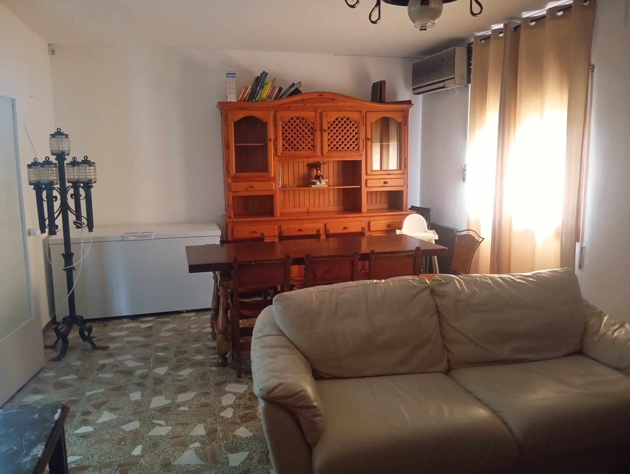 Un soggiorno con un divano, un mobile in legno pieno di libri, una lampada e un termosifone.