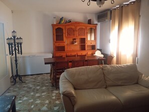 A living room with a sofa, a wooden cabinet with books, a lamp, and a radiator. - Holiday Home 'Calafell' with Mountain View, Wi-Fi and Air Conditioning (SEGUR DE CALAFELL)