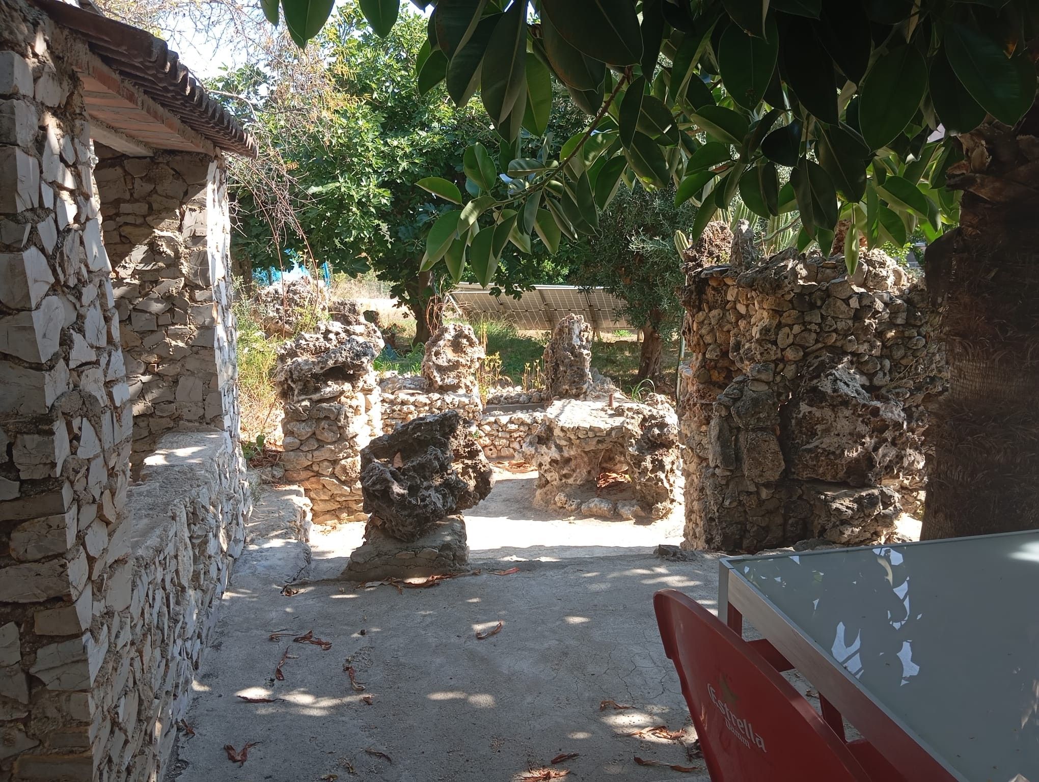 An outdoor archaeological site with stone ruins, a paved path, and a red sign.
