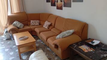 Uma sala de estar com um sofá marrom, uma mesa de centro de madeira, um sofá branco e uma mesa de mármore com revistas e canetas.
