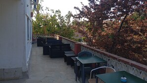 An outdoor seating area with tables and chairs, a stone floor, and a railing.