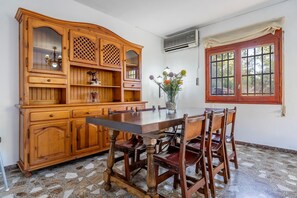 A dining area with a wooden table and chairs, a cabinet with glass doors, a vase with flowers, and a window with curtains.