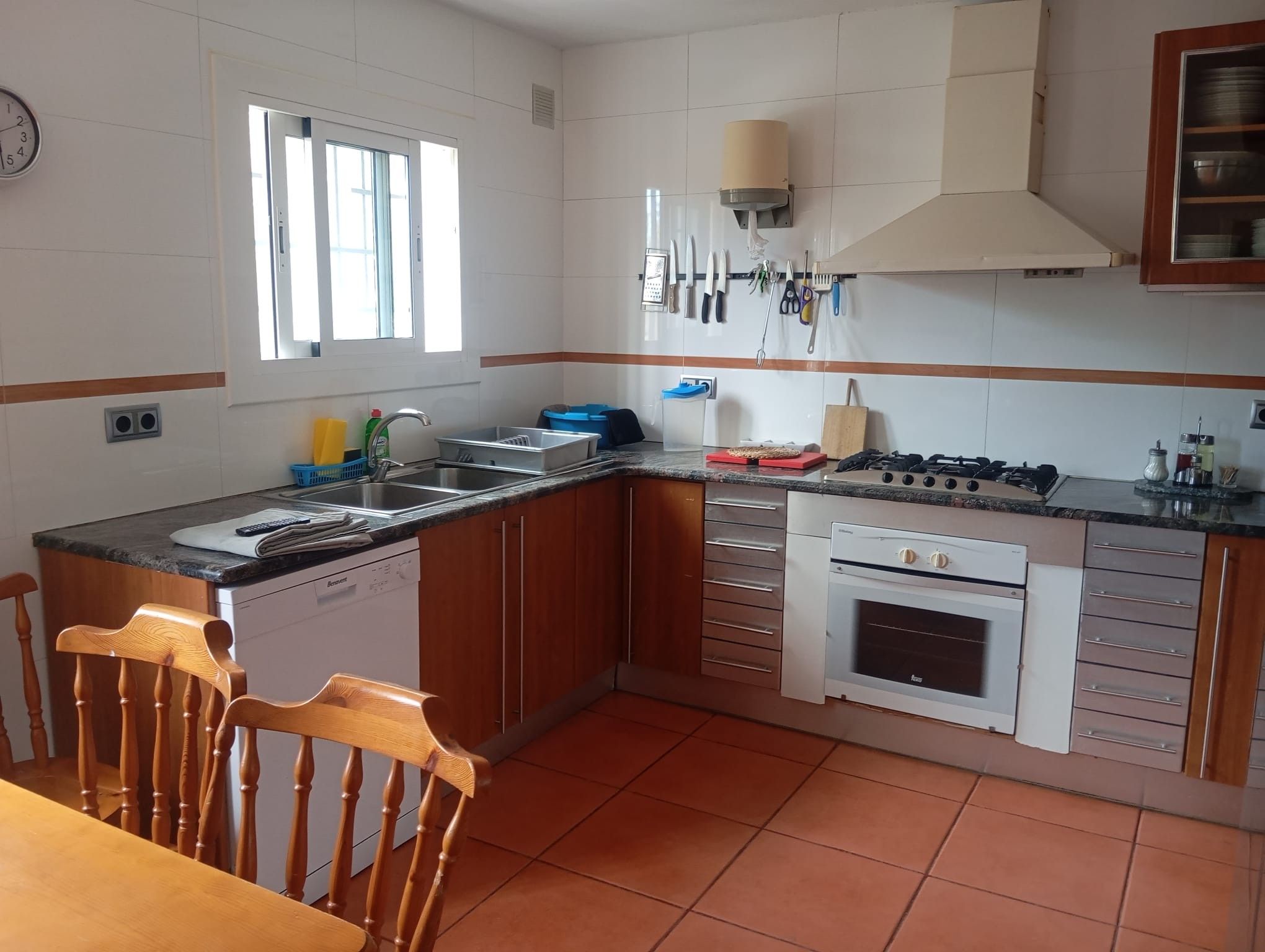 A kitchen with a gas stove, oven, sink, and wooden chairs.