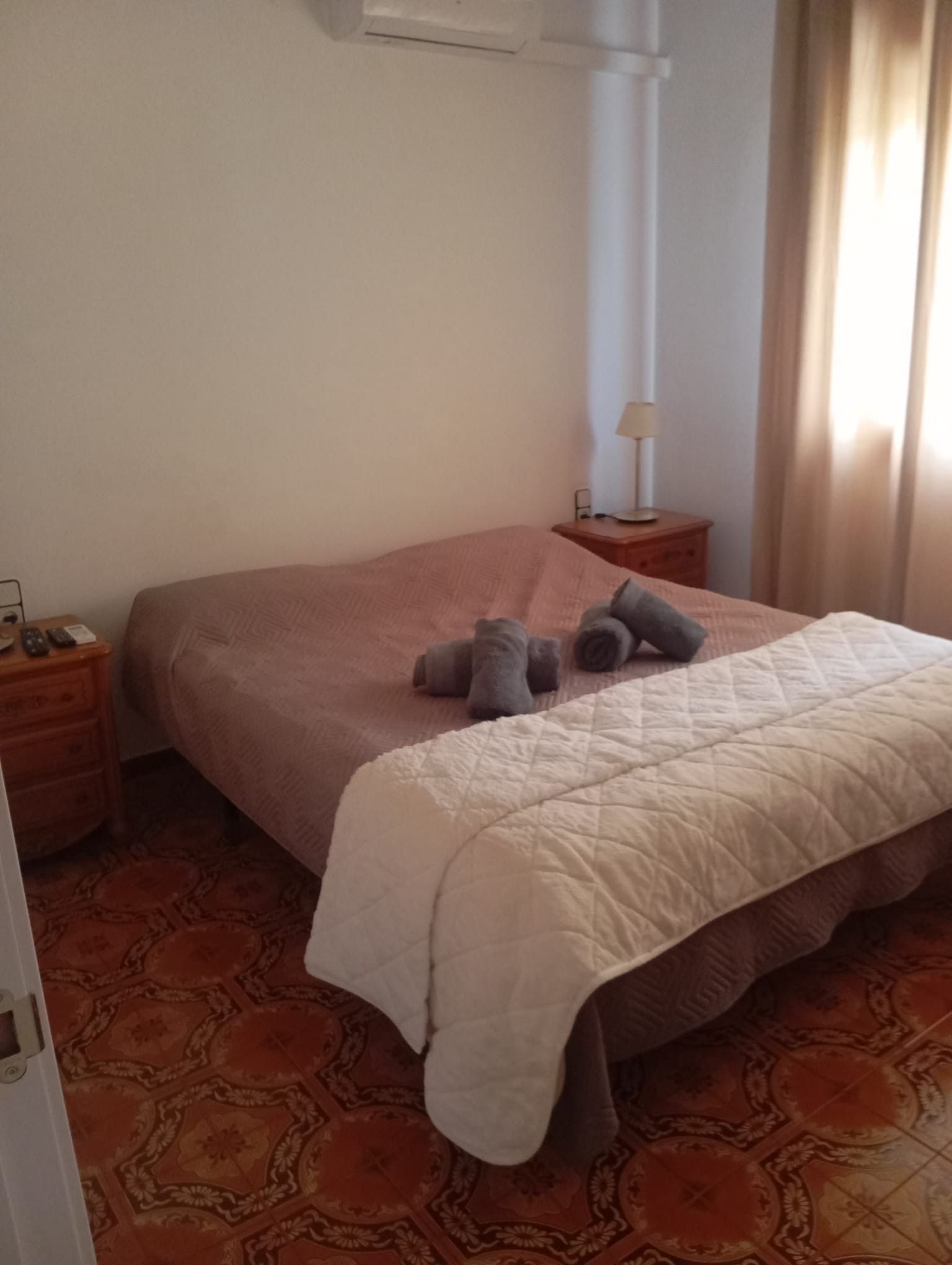 Una habitación de hotel con cama, mesita de noche, lámpara y alfombra estampada.