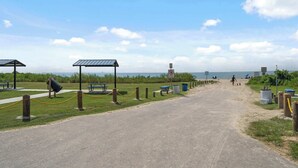 Un sentier bordant la plage qui mène aux installations balnéaires, notamment un espace de repos abrité et des tables de pique-nique.