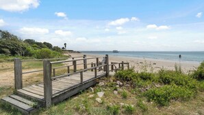Une promenade en bois qui mène à une plage, avec une jetée visible au loin et une personne dans l’eau.