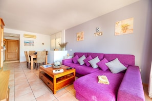 A living room with a purple sofa, wooden coffee table, and a dining area with chairs and a table.