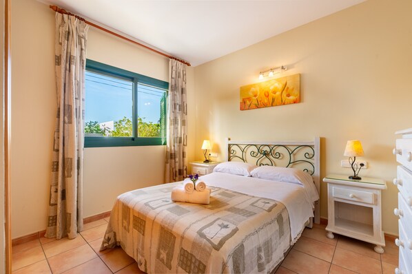 A hotel room with a bed, two bedside tables with lamps, a painting on the wall, and a window with curtains. - Apartment 'Es Pujols' with Private Terrace, Wi-Fi and Air Conditioning (Es Pujols)