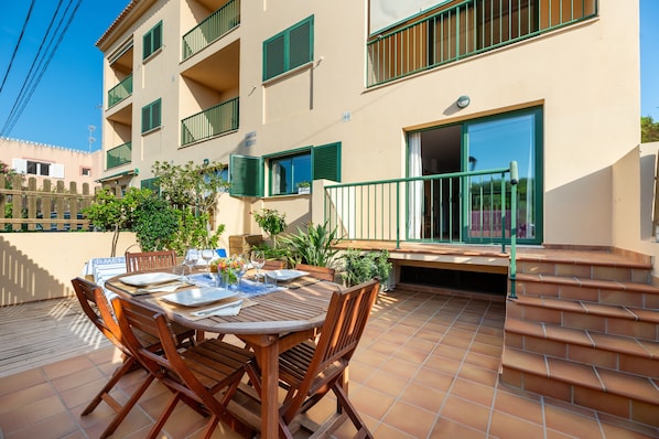 A multi-story building with balconies, a dining area with outdoor furniture, and a staircase leading to an entrance.