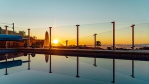 A swimming pool with a sunset in the background, surrounded by a fence and palm trees. - Vacation Home "Casa La Viña" with Sea View, Private Pool & Wi-Fi (Puntagorda)