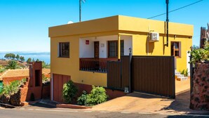 A yellow building with a gated entrance, a small porch, and a view of the ocean. - Vacation Home "Casa La Viña" with Sea View, Private Pool & Wi-Fi (Puntagorda)