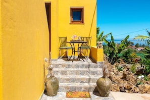 A yellow building with a small table and chairs outside, stone steps, and two large vases.