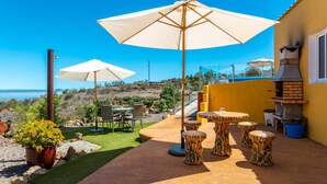 Une terrasse extérieure avec une table et des chaises, un barbecue et des parasols.
