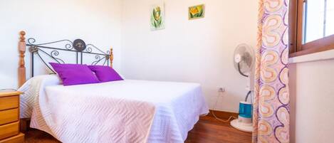A bedroom with a bed, a nightstand, a wall-mounted fan, and a window with curtains.