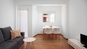Un soggiorno con un divano, un tavolo da pranzo con sedie, una televisione e una finestra con vista sugli edifici.