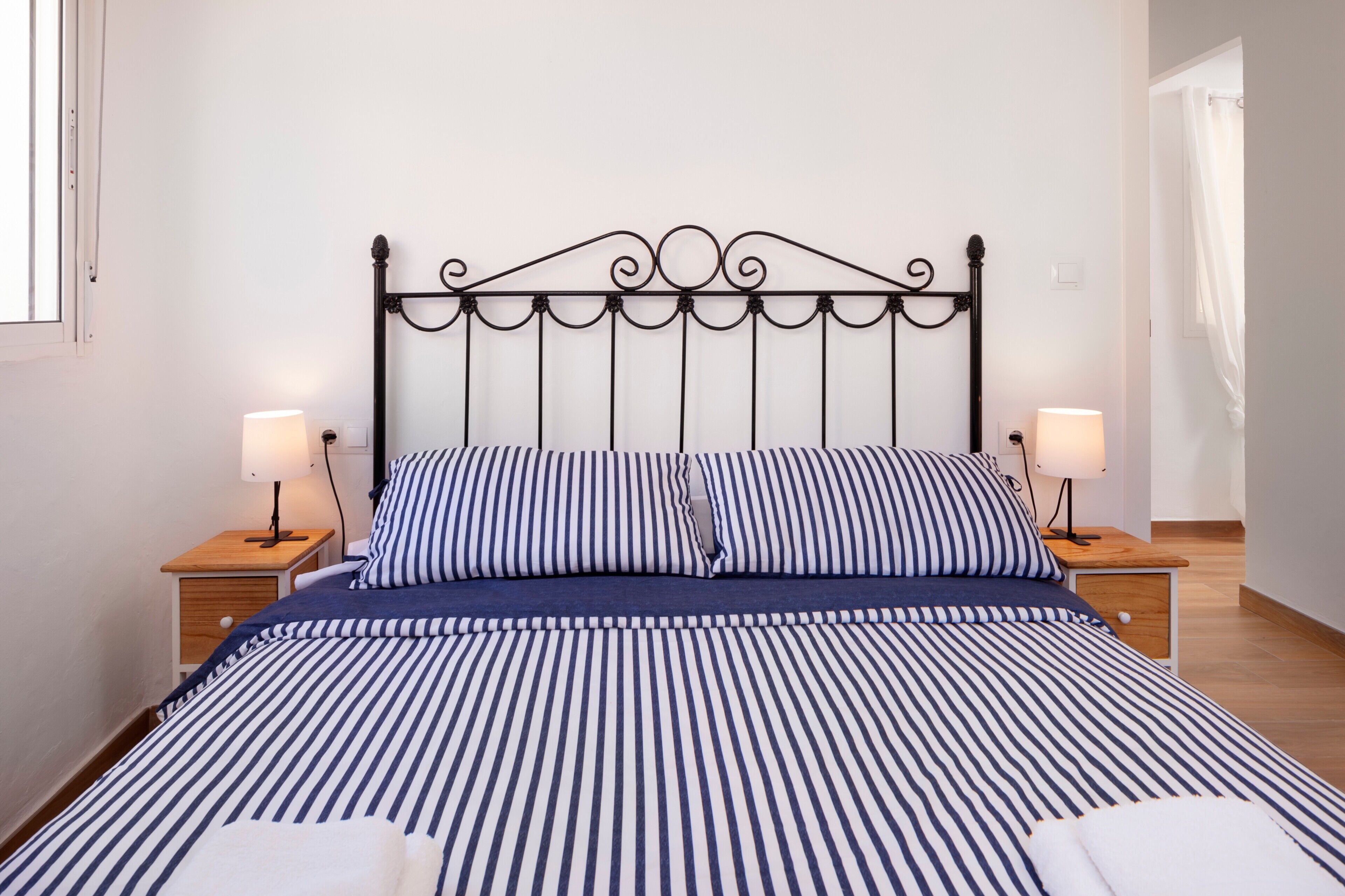 A neatly made bed with striped bedding, two bedside tables with lamps, and a simple headboard.