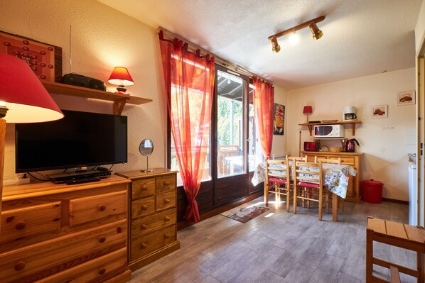 A room with a television, wooden furniture, a dining table, and a kitchen area.
