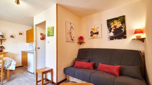 Un accogliente soggiorno con un divano, un piccolo tavolino e una zona cucina visibile attraverso una porta aperta.