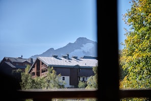 Un edificio de madera tradicional con techo inclinado, rodeado de vegetación y montañas al fondo.