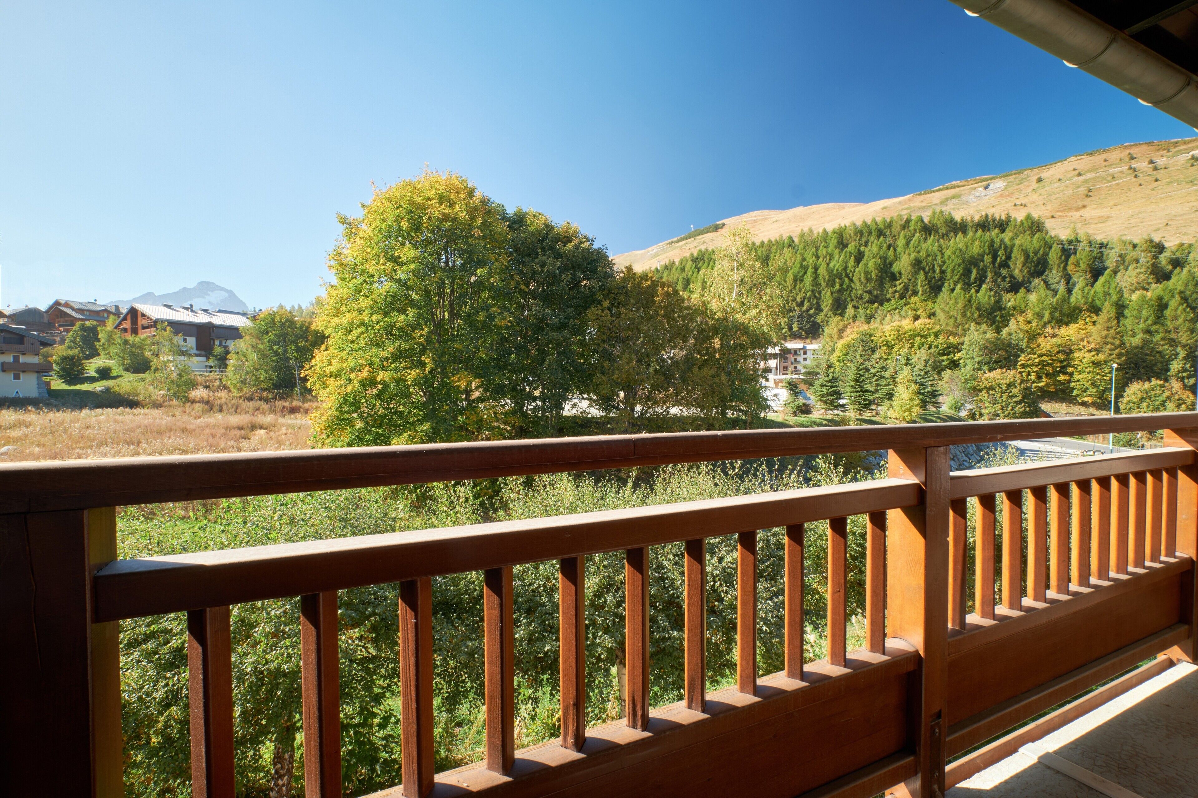 A balcony with a wooden railing overlooking a mountainous landscape with trees and buildings.