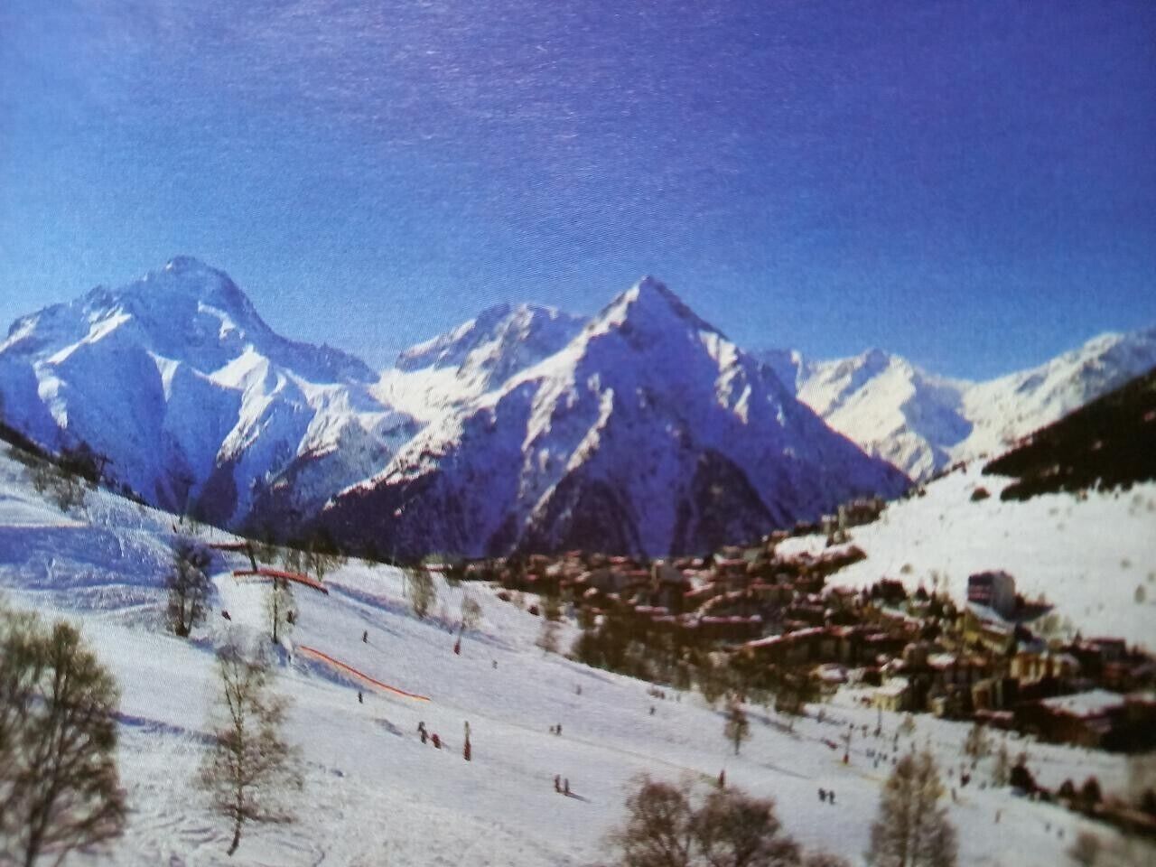 A snowy mountain landscape with a ski slope, a small village, and snow-covered peaks.