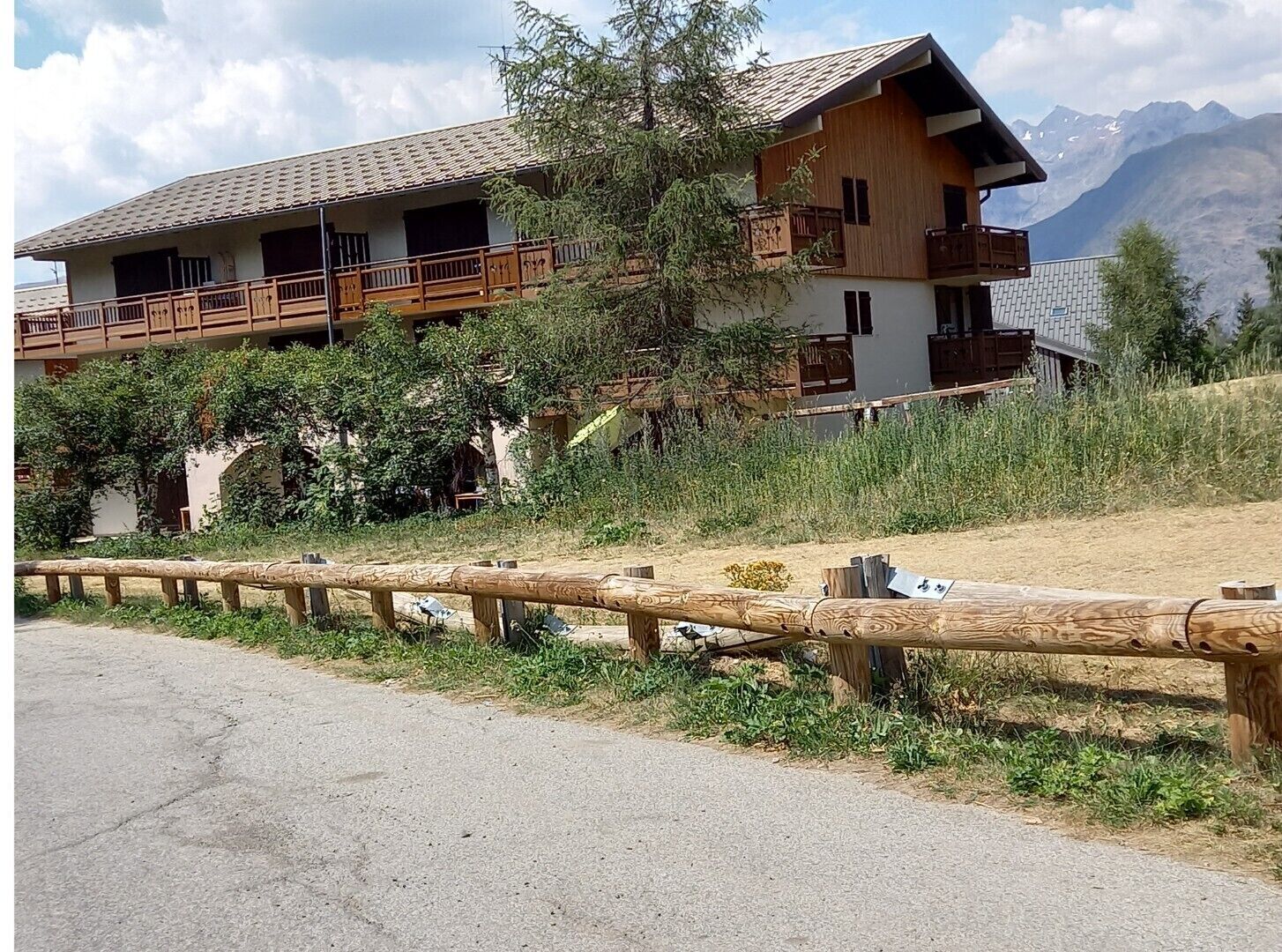A two-story wooden building with balconies, surrounded by greenery and mountains in the background.