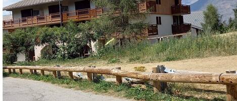 A two-story wooden building with balconies, surrounded by greenery and mountains in the background.