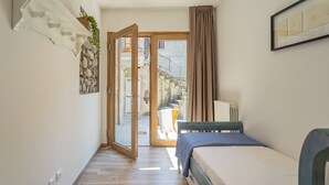 Ein Schlafzimmer mit Bett, einem fenster mit Vorhängen, einer Tür zu einem Außenbereich und einem an der Wand befestigten Regal mit einer Pflanze.