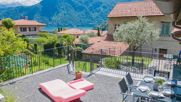 Eine Terrasse mit Außenbestuhlung und einem Esstisch, mit Blick auf eine Berglandschaft und einen See.