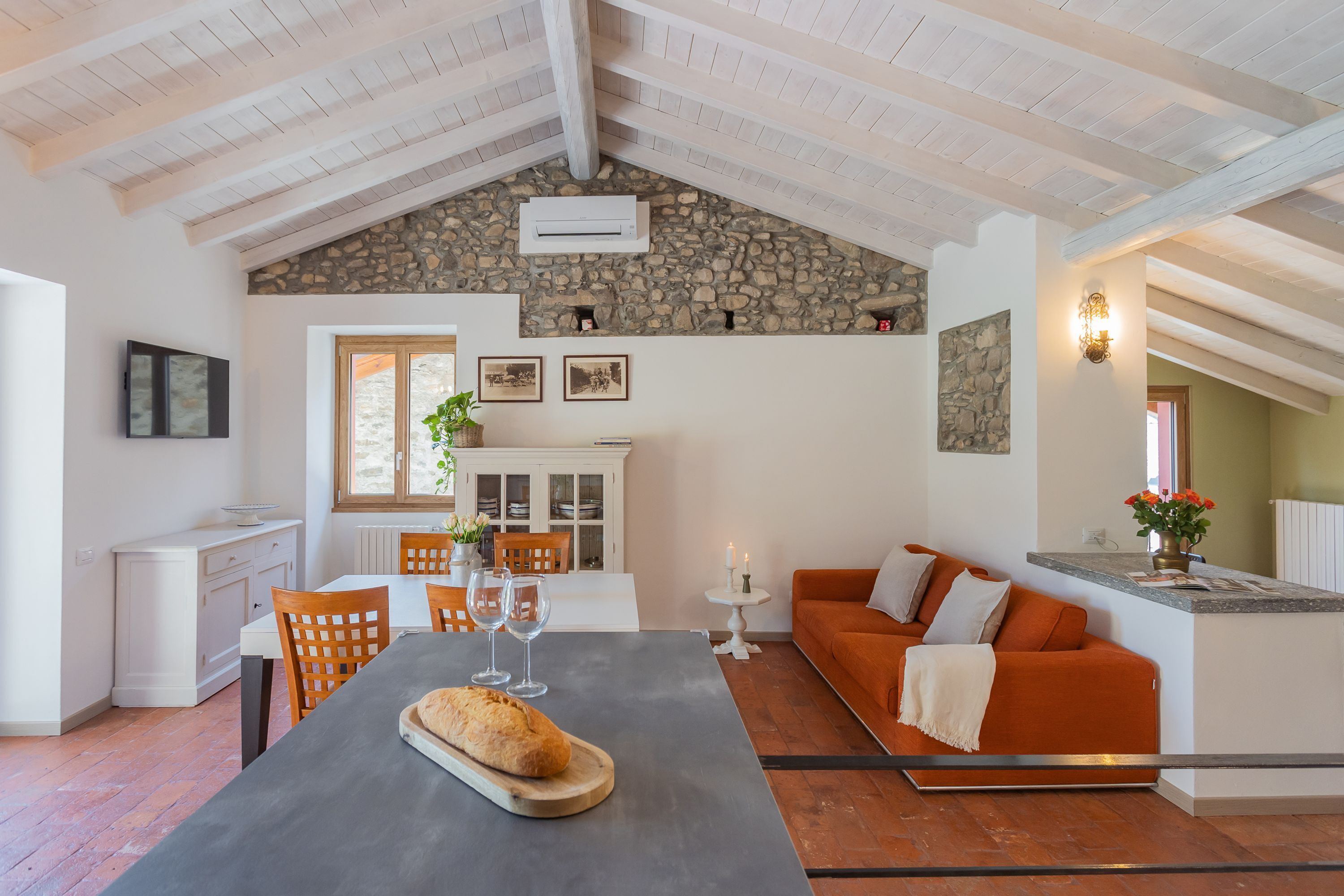 A spacious living area with a stone ceiling, a dining table with chairs, a sofa, and a kitchen area with a white cabinet and a window.