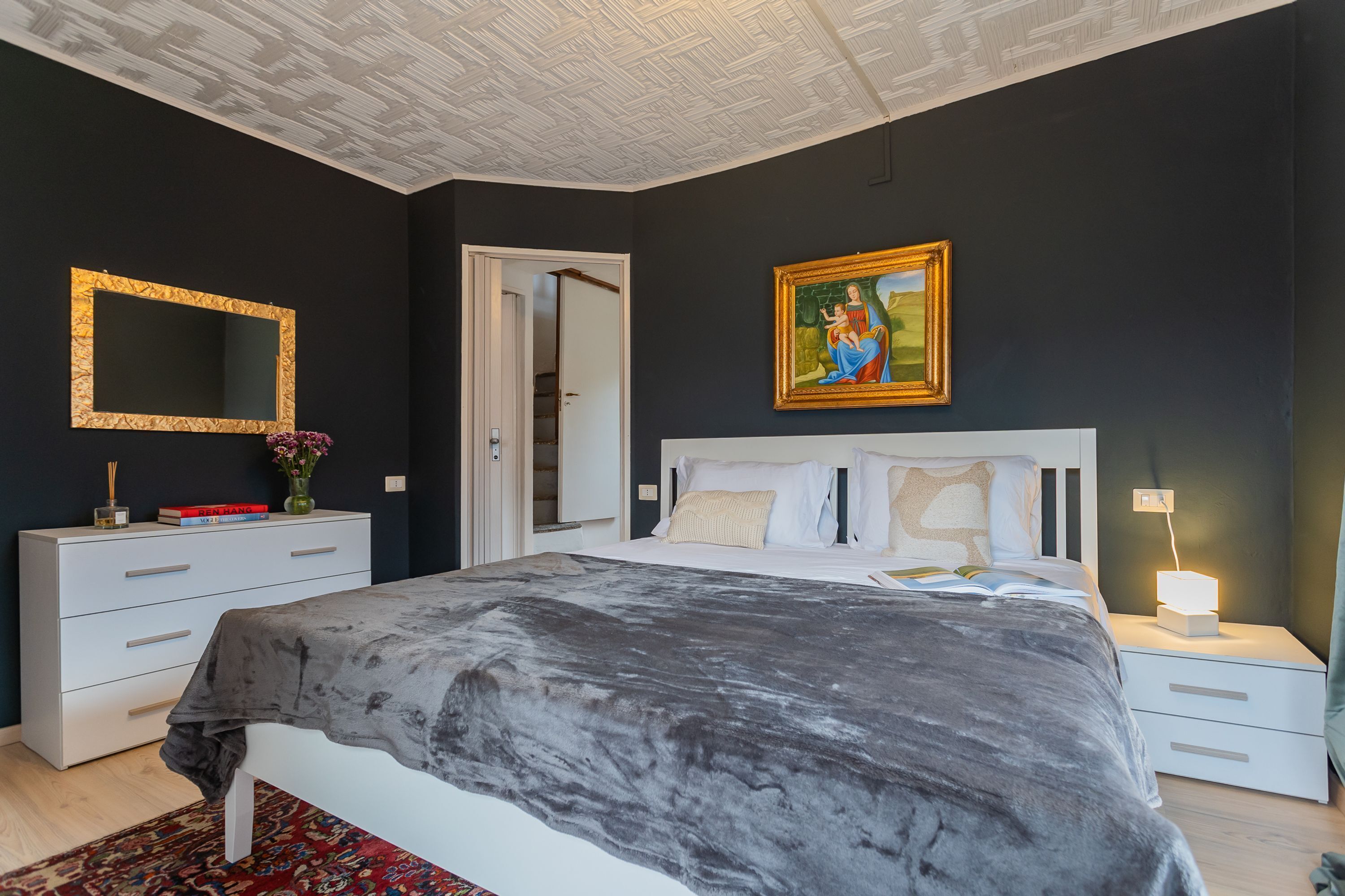 A bedroom with a bed, bedside tables, a nightstand, a mirror, and a painting on the wall.