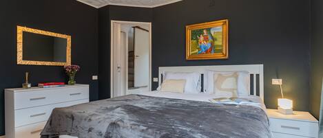 A bedroom with a bed, bedside tables, a nightstand, a mirror, and a painting on the wall.