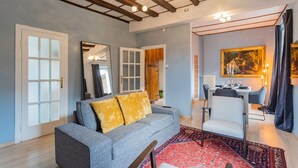 Uma sala de estar moderna com um sofá cinza, um tapete estampado em vermelho e uma área de jantar com mesa e cadeiras.