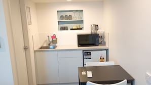 Una kitchenette compacta con microondas, cafetera y un lavamanos pequeño.