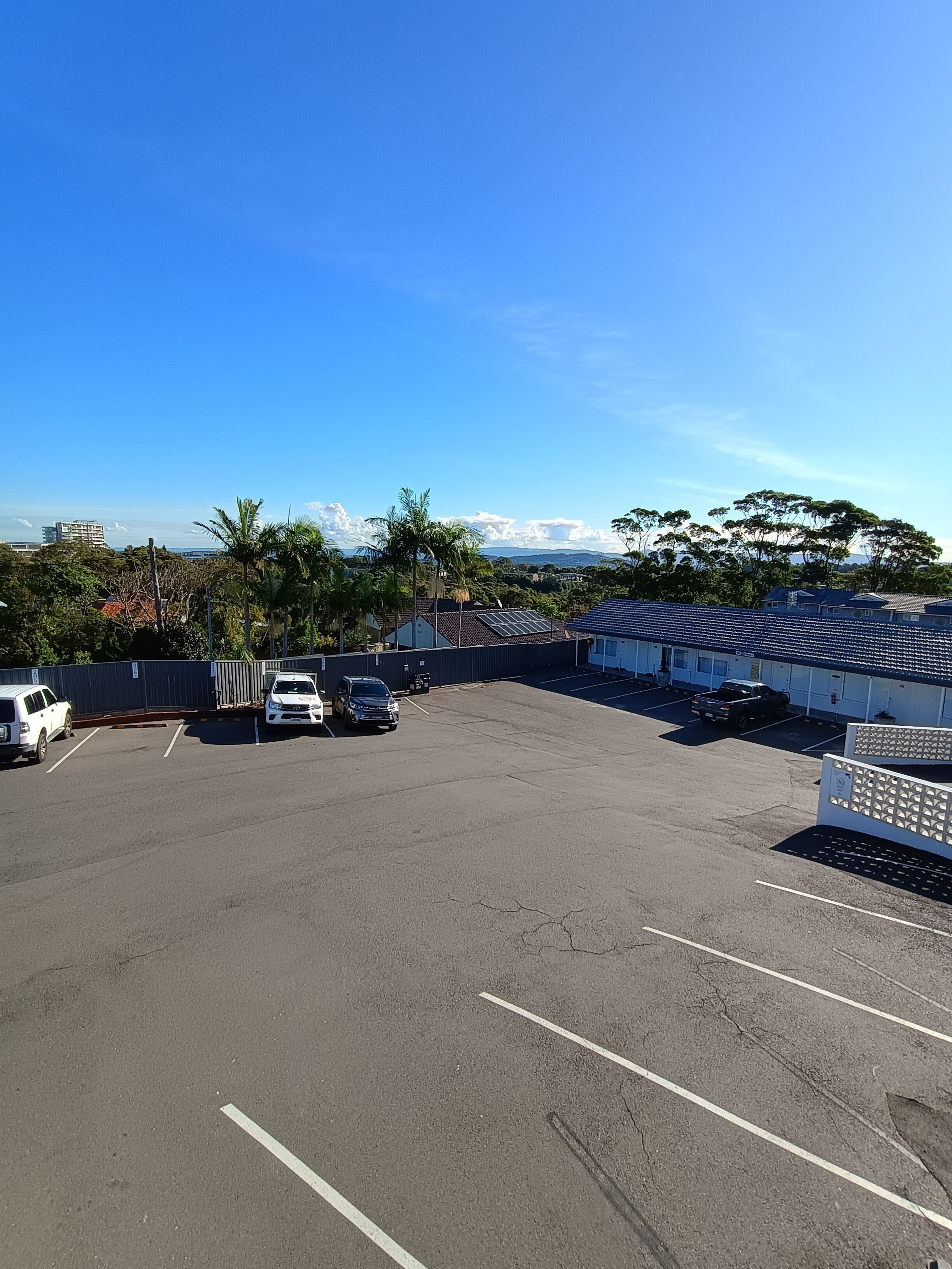 A parking lot with several cars, a building with a blue roof, and a clear blue sky.